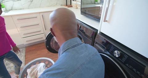 African american man and young woman doing laundry in modern home with marble backsplash