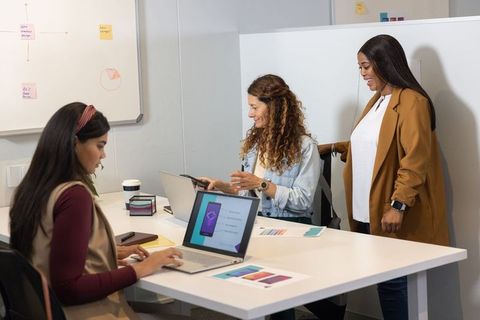 Multiracial female team collaborating on app design with laptops, tablet, color swatches