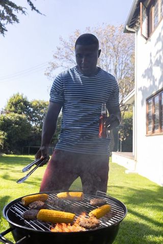 Man grilling corn and burgers in sunlit backyard