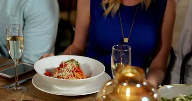 Woman in blue dress dining with pasta and champagne - Download Free Stock Images Pikwizard.com