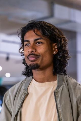 Indian young man smiling and looking right in cafe wearing bomber jacket and ear stud