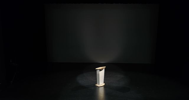 Podium illuminated by bright spotlight in otherwise dark theater. Ideal for themes relating to public speaking, presentations, performance anxiety, or motivational speech events. Also suitable for use in marketing for conference and seminar promotions, theater advertisements, or blog posts about overcoming stage fright.