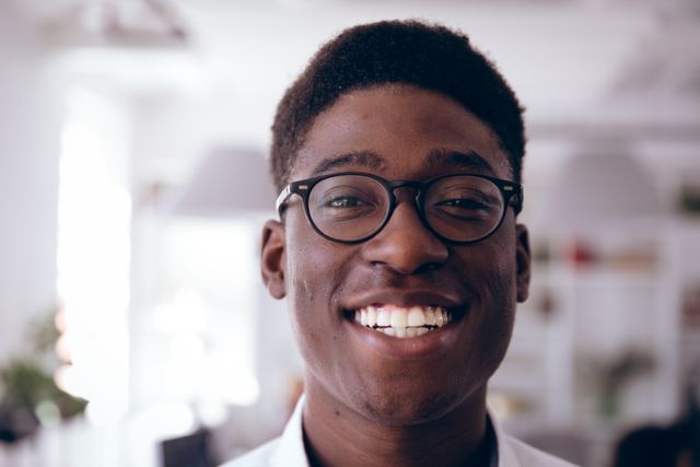 Portrait of happy African American professional businessman working in a modern creative office, wearing glasses and looking at camera smiling. Business office creativity.