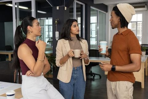 Colleagues discussing over coffee in modern open-plan office, collaborating casually during break