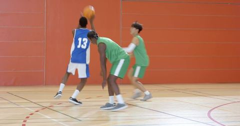 High school basketball players driving to hoop while defenders lunging in indoor game