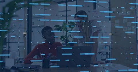 Two women collaborating over laptop with blue digital overlay in modern coworking office
