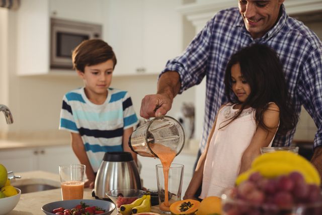 Father preparing smoothie with his kids in kitchen at home