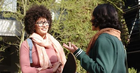 College Friends Chatting Smiling Outdoors Holding Skateboard and Backpack on Sunny Campus