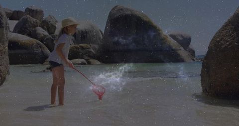Child exploring rocky beach cove with net under starry sky
