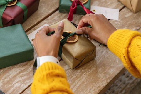 African american hands tying green ribbon on gold gift with dried orange, mustard knit