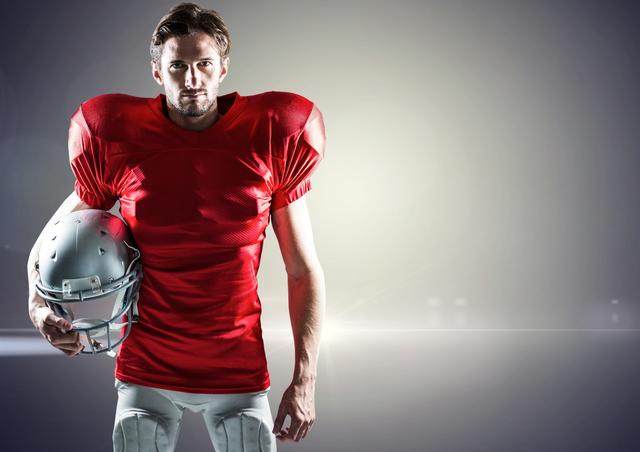 Male American football player standing confidently while holding a helmet. Ideal for use in sports advertisements, athletic promotions, team spirit campaigns, and fitness-related content.