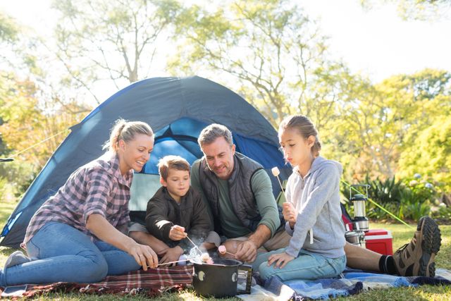 Family enjoying outdoor camping trip, roasting marshmallows together. Perfect for promoting family bonding, outdoor activities, camping gear, summer vacations, and nature adventures.
