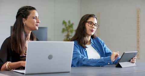 Diverse female colleagues collaborating over laptop and tablet at modern office table