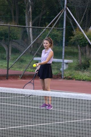 Female tennis player standing ready in purple top and skirt on outdoor hard court