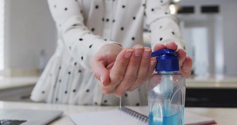 Woman using hand sanitizer in modern kitchen