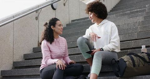 Multicultural friends sitting on campus steps sharing phone after outdoor workout