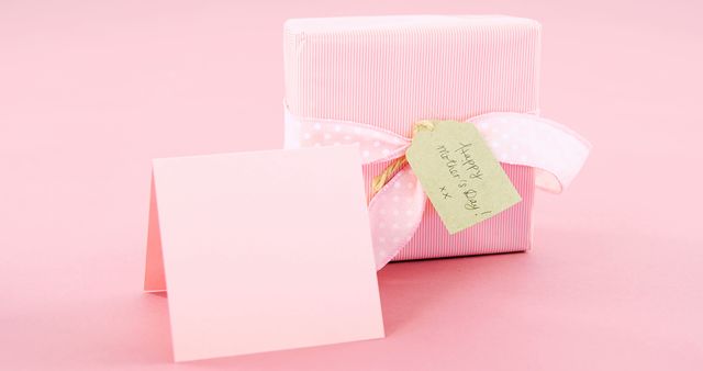 A pink gift box with a white ribbon and a tag reading Mother's Day rests on a matching pink background, with copy space. Perfect for conveying the warmth of a Mother's Day celebration and the tradition of gift-giving.