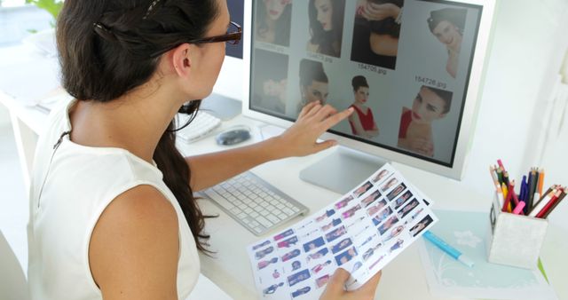 Fashion designer uses computer for analyzing clothing samples while holding printed designs. Useful for projects on fashion design, creativity, digital workspaces, and professional industries showcasing the innovation process in the fashion sector.