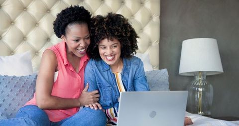 Women Laughing Together While Using Laptop at Home Relaxed