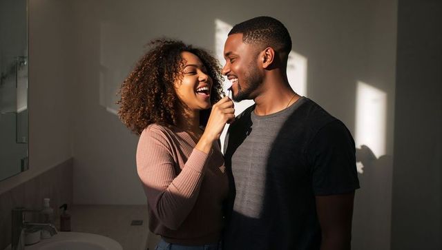 Black couple brushing teeth together in sunlit modern bathroom, playful morning routine