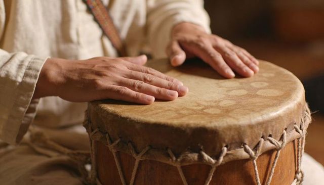 Hands tapping rope-tuned wooden drumhead, playing traditional hand drum rhythms, warm closeup
