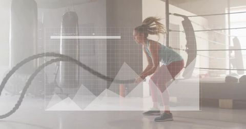 Woman swinging battle ropes in boxing gym with digital graph overlay for fitness training