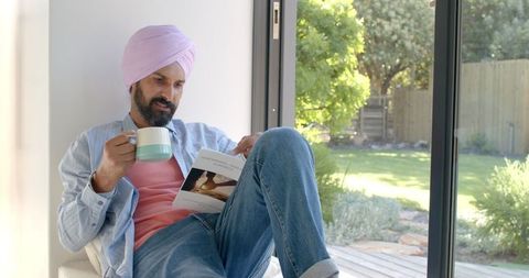 Man relaxing at home with coffee and magazine by sunlit window