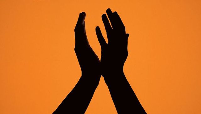 Raising mirrored hands forming dramatic black silhouette against vibrant orange backdrop