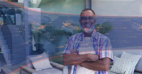Mature man standing with crossed arms in modern apartment with city lights reflections