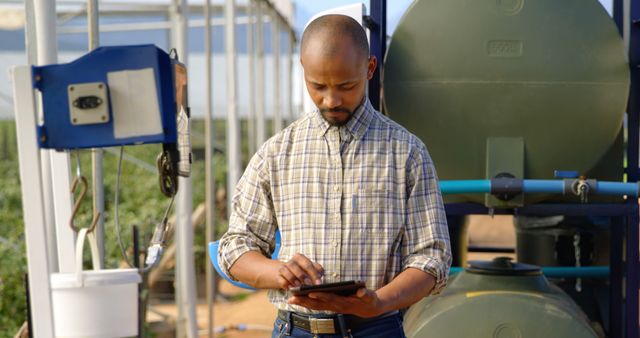 A man is using a tablet in a greenhouse or farm environment, focusing on modern agricultural technologies. This can be used in articles related to agritech innovations, agricultural engineering, sustainable farming methods, or showcasing advanced farming techniques. It can also serve as a visual aid in presentations on modern agriculture and tech integration on farms.