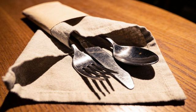 Cutlery tucked in linen napkin casting warm shadows on wooden table with rustic texture