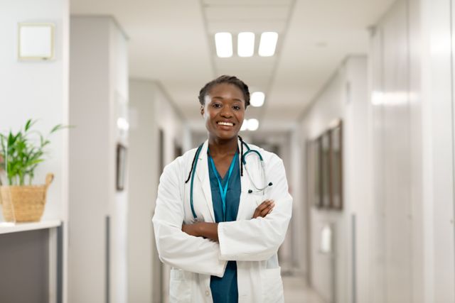 Portrait of smiling african american female doctor standing in hospital corridor, with arms crossed. Medical services, hospital and healthcare concept.