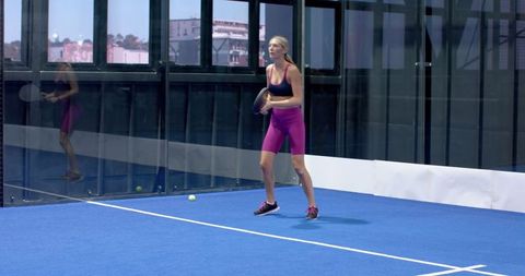 Female Athlete Playing Padel on Blue Court with Glass Walls
