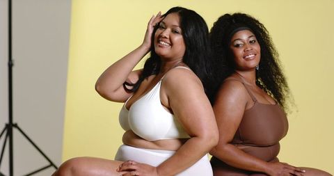 Confident diverse plus-size models posing back-to-back in lingerie on yellow backdrop