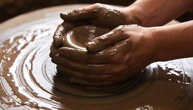 Hands centering and shaping wet clay on spinning pottery wheel, close-up of craftsmanship