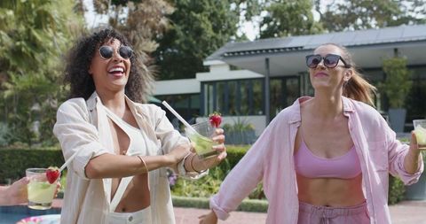 Friends laughing and dancing while holding cocktails poolside backyard summer celebration
