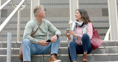 Mature couple sitting on city steps sharing coffee and flowers during casual conversation