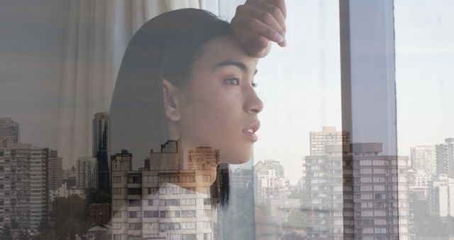 Composition of biracial woman looking out of window and cityscape. City and urban living concept.