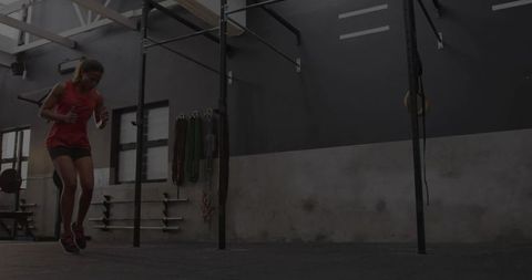 Female athlete jumping in crossfit gym with pull-up rig, rings and industrial interior