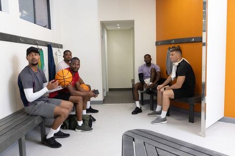 Diverse basketball teammates sitting in locker room preparing for game and team huddle