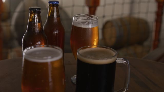 Variety of beers displayed in bottles and glasses on a wooden bar at a microbrewery pub featuring different kinds of beer such as ale, lager, and stout. Ideal for use in advertising for pubs, microbreweries, beer festivals, or social gatherings celebrating craft beer. Great for illustrating the diversity of beer offerings.