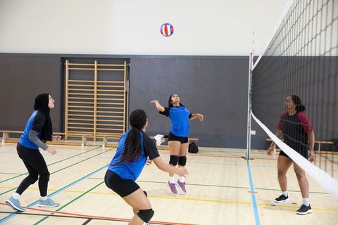 Young women volleyball team competing at net in indoor gym showing teamwork and agility