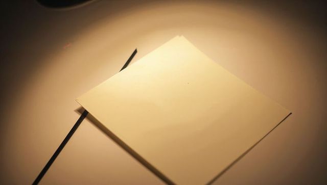 Minimalist square white card sitting diagonally on pale tabletop with black ribbon shadow