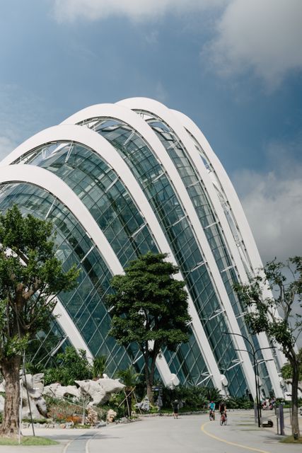 Modern glass architecture featuring a distinctive curved design with green plants and trees surrounding the structure. Ideal for use in topics related to modern urban landscapes, cutting-edge architectural design, and integration of nature with urban environments.
