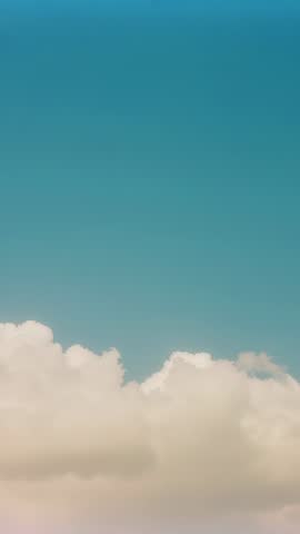Vertical video of cumulus cloud bank drifting right across teal sky with soft horizon