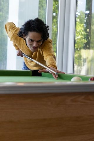 Indian man leaning over pool table aiming cue for precise shot in bright home interior