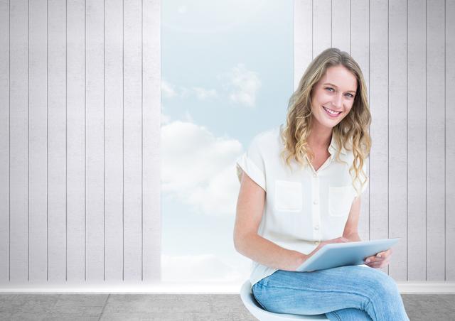Young woman sitting on a modern chair, using a tablet. She is smiling cheerfully with a bright, open sky and clouds visible through a vertical opening in the background. Perfect for themes of technology use, modern lifestyle, relaxation, and work-from-home conditions.