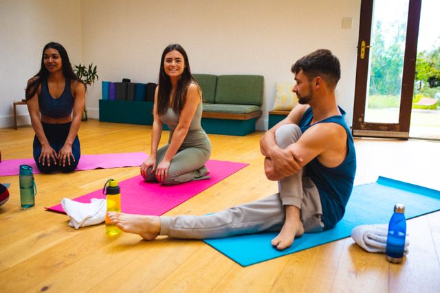 Multiracial fit young man and smiling women talking while doing stretching exercise at yoga studio. unaltered, fitness, yoga and healthy lifestyle.