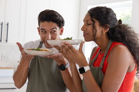 Couple savoring aroma of homemade bowls while wearing aprons in bright sunlit kitchen