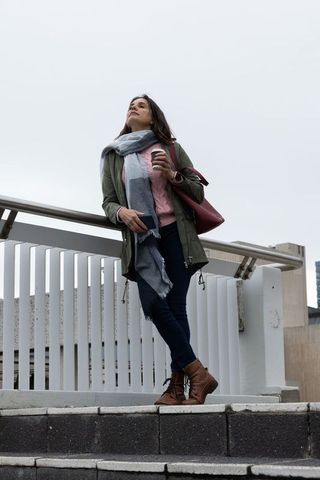 Woman leaning on handrail holding coffee and smartphone on urban overpass cloudy day